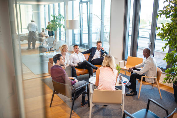 Working Group Portrait of Businesspeople in Office Lobby Elevated personal perspective photographed through window of diverse business colleagues relaxing and talking in modern office lobby. business relationship stock pictures, royalty-free photos & images