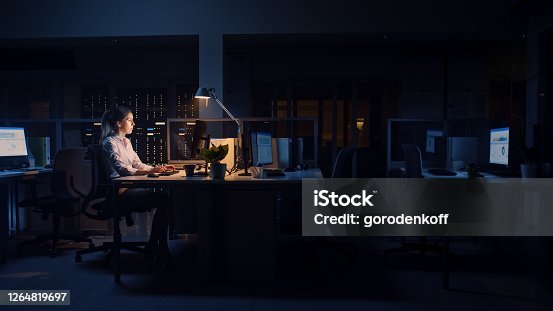 istock Working Late at Night in the Office: Businesswoman Uses Desktop Computer, Analyzing, Using Documents, Solving Problems, Finishing Important Project. Diligent Ambitious Young Worker. Side View 1264819697