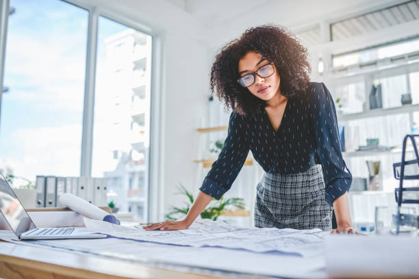 Working on a few high-class designs Shot of a young businesswoman working with blueprints in an office architect stock pictures, royalty-free photos & images