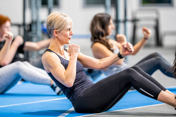 Working out together in a class A middle aged caucasian woman shows a look of determination as she does an ab workout with a group of people in a gym. 40 49 years photos stock pictures, royalty-free photos & images