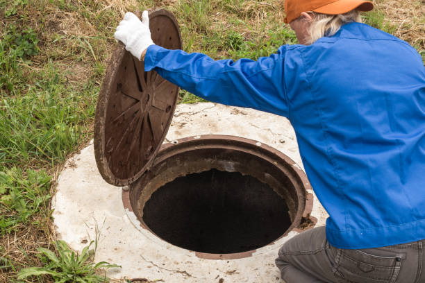 A working plumber opens a sewer hatch. Maintenance of septic tanks and water wells stock photo