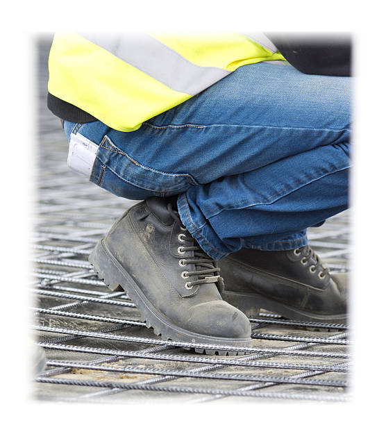 Engineer in working shoes squatting on reinforcement mesh at...