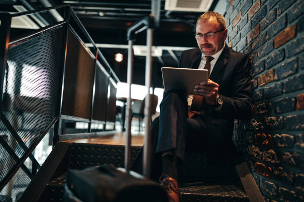 Working while on the move Mature businessman sitting on a staircase , holding a tablet Portable DVD Player stock pictures, royalty-free photos & images