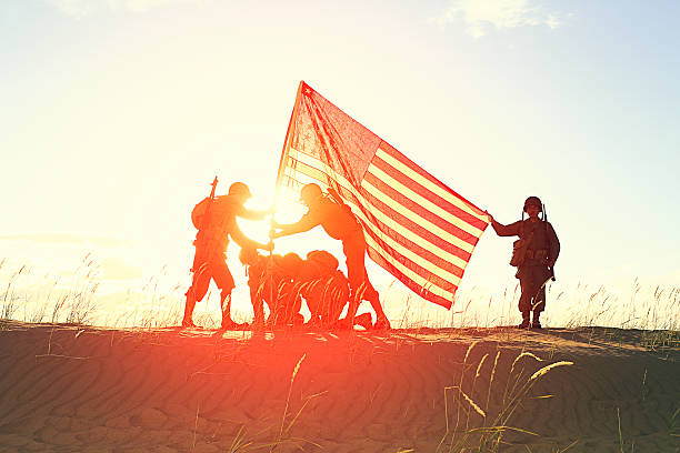 Five WW2 Army soldiers raise the American flag as the sun sets behind them. Authentic World War 2 uniforms and flag. Great photo for US Veteran's Day. More vintage military photos.
