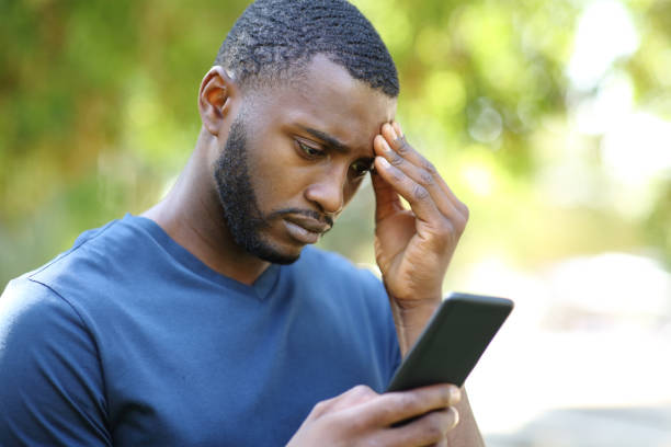 Worried black man checking smart phone in a park stock photo