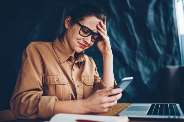Worried hipster blogger crying while reading incoming sms message with bad news on smartphone device.Frustrated young woman making mistake during installing new application on telephone via internet stock photo