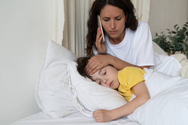 Worried mother call to doctor checking temperature of sick kid lying in bed. Child cure and health stock photo