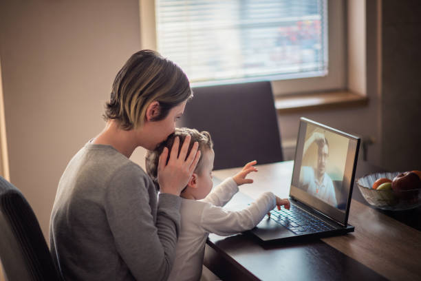 madre preoccupata che bacia la testa del bambino durante la sua videochiamata con il padre separato - kostic foto e immagini stock