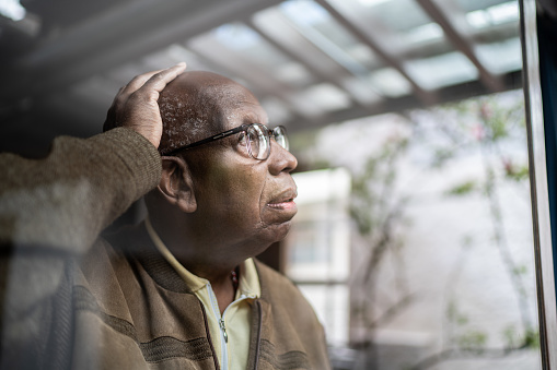 Worried senior man looking through the window at home