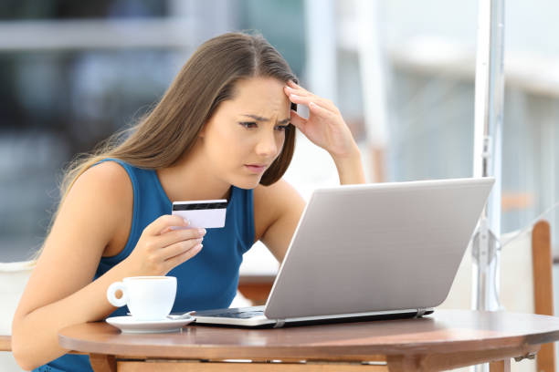 Worried shopper paying with credit card Worried on line shopper trying to pay with a credit card and a laptop sitting in a bar terrace online fraud in restaurants stock pictures, royalty-free photos & images