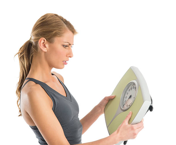 Worried Woman Looking At Weight Scale stock photo