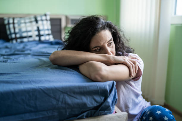 Worried woman sitting on floor next to bed stock photo