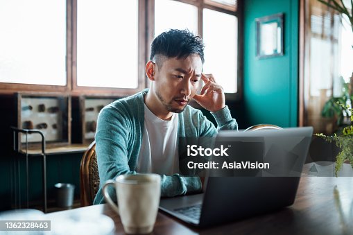 istock Worried young Asian man with his hand on head, using laptop computer at home, looking concerned and stressed out 1362328463