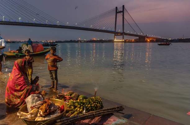 Worship April 11,2019. Kolkata, India. An Unidentified Indian woman with Puja Thali, worship River Ganges at Prinsep Ghat, overlooking Vidyasagar Setu/ Second Hooghly Bridge. chhath stock pictures, royalty-free photos & images
