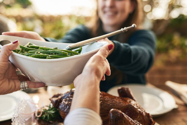 Would you like some greens? Shot of a unrecognizable woman passing on a plate of green beans to a cheerful woman at lunchtime over a table thanksgiving food stock pictures, royalty-free photos & images