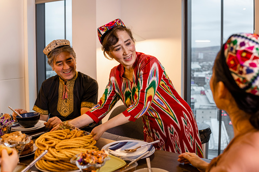 A multi-generation Uyghur family wearing traditional clothing and Doppa's, a traditional hat of the Uyghurs. They are enjoying food at the dining table to celebrate Eid al-Fitr the end of Ramadan.
