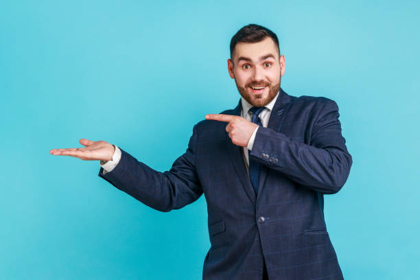 Wow, look at commercial proposal! Bearded man in suit pointing at copy space on palm, showing empty place for idea presentation, product advertising. stock photo