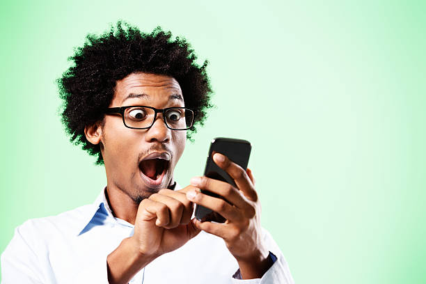 Wow! This phone can do everything! A young geek with an afro and horn-rimmed glasses looks down, amazed as he discovers just what his smartphone can do!. smart phone green background stock pictures, royalty-free photos & images