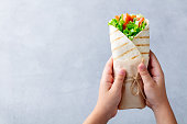 Wrap sandwich in kids hands. Grey stone background. Top view. Copy space.