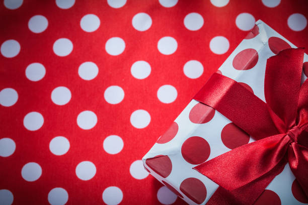 Wrapped gift box with bow on polka-dot red table cloth holidays...