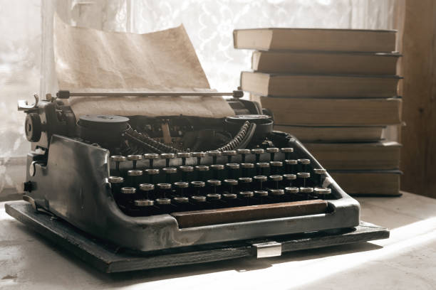 Writer. Typewriter with blank page and a stack of books on a writer table background. typewriter stock pictures, royalty-free photos & images