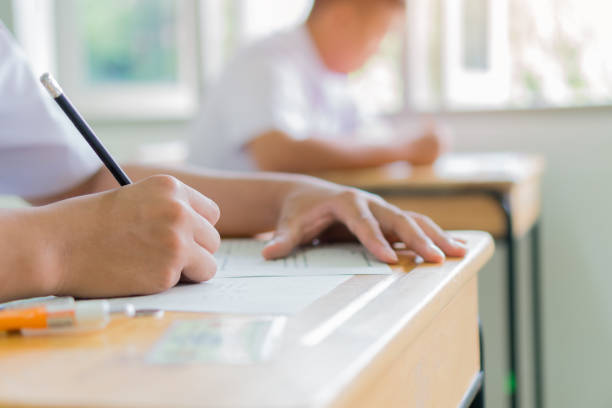 Writing test in exam Asian students concentrate in high school, serious taking final examination desk at classroom with Thai student uniform. Back to school for evaluation after COVID-19 pandemic stock photo