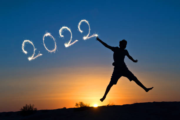 2022 written with sparkles, silhouette of a boy jumping in the sun, new year card stock photo