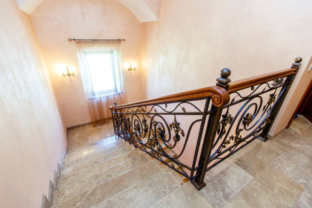 wrought iron staircase in the cottage. Marble steps, black wrought iron stairs with floral ornaments. Mahogany wooden railing. wrought iron staircase in the cottage. Marble steps, black wrought iron stairs with floral ornaments. Mahogany wooden railing. The staircase between floors of the cottage bannister stock pictures, royalty-free photos & images
