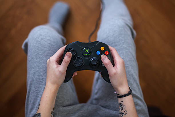 Xbox game controller - Microsoft Xbox Gothenburg, Sweden - January 24, 2015: A shot from above of a young womans hands holding a game controller for the Microsoft Xbox, a video game console. Natural lighting. Shot on wooden background with shallow depth of field.  xbox photos stock pictures, royalty-free photos & images
