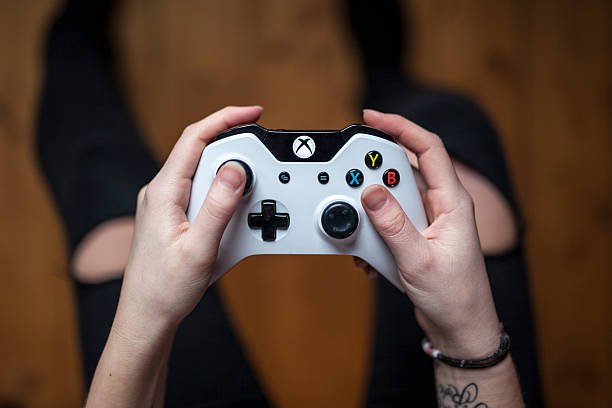 Xbox One Controller - White Gothenburg, Sweden - January 17, 2015: A shot from above of a young woman's hands holding a white Xbox One controller as she is playing a video game. Natural lighting, shot on wooden background with shallow depth of field. xbox photos stock pictures, royalty-free photos & images