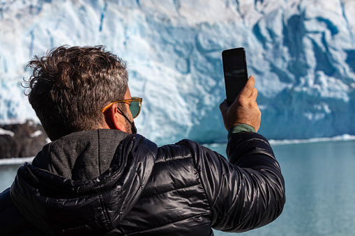 Unrecognizable person photographing Glacier Perito Moreno from boat