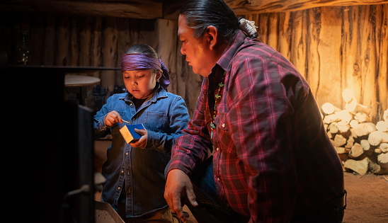 Indigenous navajo 10 years old with his dad trying to start the fire on a  traditional stove inside a hogan