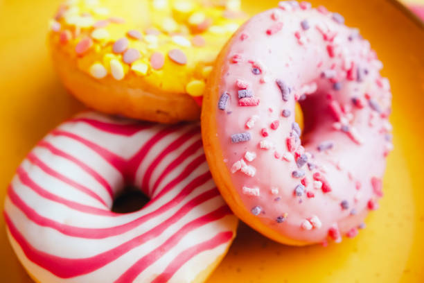 Yellow and pink sugar glazed donuts on colorful purple background. stock photo