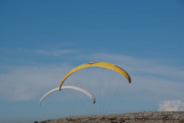 Two Paragliders Flying Above the Beach Seattle, Washington, USA - April 13, 2012: Yellow and white paragliders Fly above the beach at Golden Garden Park on a sunny day. jeff goulden paragliding stock pictures, royalty-free photos & images