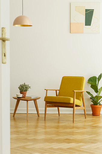 Yellow armchair and coffee table with a cup and plant on a herringbone parquet in a living room interior. Real photo