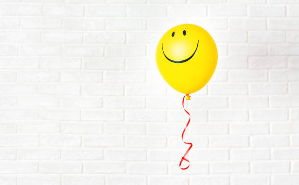 yellow ballon with smile hangs aganst white wall - comemoração conceito imagens e fotografias de stock