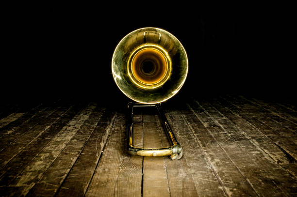 yellow brass instrument trombone lies on the wooden floor of the stage. front view on the bell yellow brass instrument lies on a wooden floor in the dark wind instrument stock pictures, royalty-free photos & images
