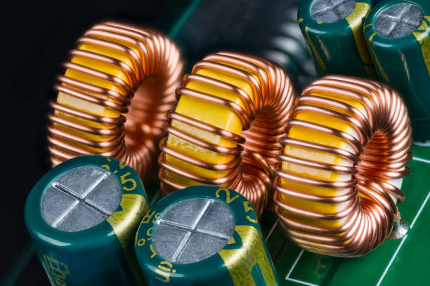 Yellow ferrite cores of toroidal inductors wrapped with copper wire on green printed circuit board stock photo