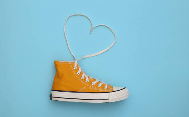 Yellow high-top sneaker (gumshoe) with untied heart shaped laces on blue background. Top view. Love concept stock photo