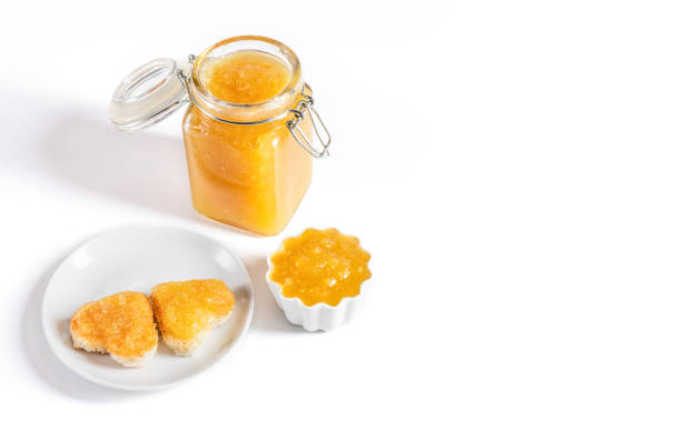 Yellow jam and toast hearts on a white background. Fruit confiture in a jar. Copy space. stock photo