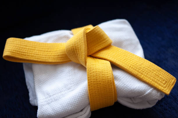 Yellow judo, aikido, or karate belt, tied in a knot on white kimono Yellow judo, aikido, or karate belt, tied in a knot on white kimono bushido lifestyle stock pictures, royalty-free photos & images