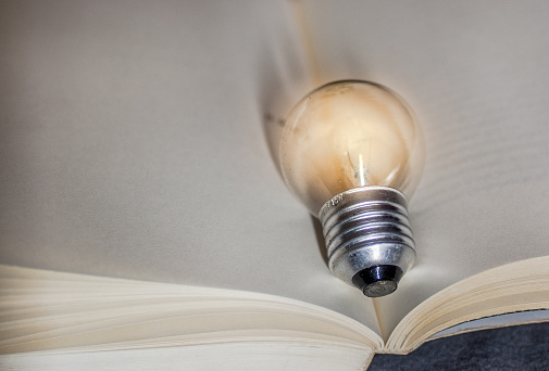 Yellow Light Bulb Lamp Over Open Blank White Book Writing