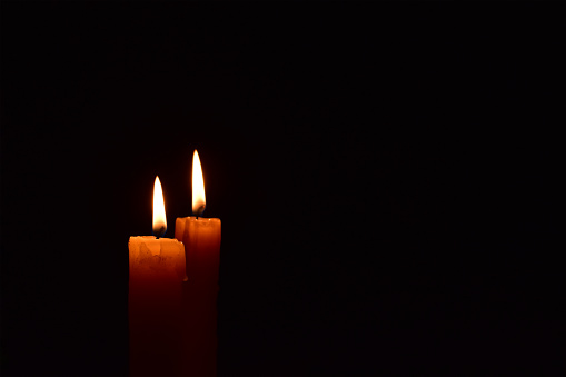 Old yellow light candle burning brightly in the black background. Candle flame. There's room for your text. Light in darkness.