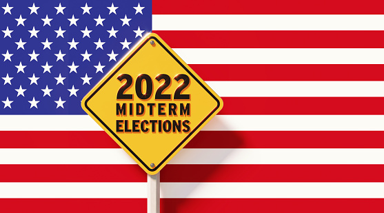 Yellow off road traffic sign with 20202 Midterm Elections ahead text in front of American flag. Horizontal composition with copy space.