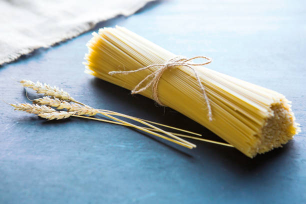 yellow raw spaghetti on a blue wooden table Spaghetti and ear wheat lying on a wooden table. uncooked pasta stock pictures, royalty-free photos & images