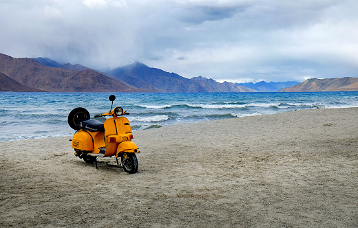 Leh Ladakh: yellow scooter from bollywood movie parking at highest salt lake in the world with mountain background at Pangong Lake