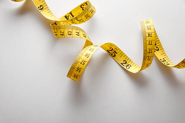 Yellow tape measure in meters and inches in a spiral Yellow tape measure in meters and inches in a spiral on white table. Top view. Horizontal composition. centimeter ruler stock pictures, royalty-free photos & images