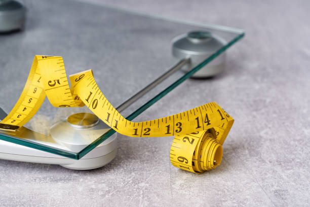 yellow tape measure on glass bathroom scale yellow tape measure on top of glass bathroom weighing scale on blue. Front view copy space. Healthy lifestyle, weight losing management and hydration concept banner obesity stock pictures, royalty-free photos & images