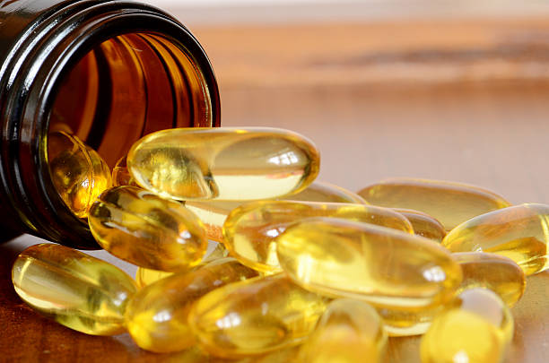 Yellow transparent capsules falling out of a brown bottle ็Heap of transparent yellow capsules pored out from amber bottle. fish oil stock pictures, royalty-free photos & images