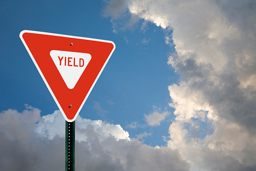 A yield sign on the left side of the frame with copy space above and to the right of the sign.  Blue sky and storm clouds in the background.